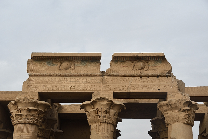 33 MAK_6340.jpg - Sul fregio decorativo sopra il portale del tempio si trova il sole alato primordiale, simbolo di protezione divina del luogo sacro attorniato da due cobra, simboli di regalità e forza distruttrice contro i nemici degli dei e del faraone.